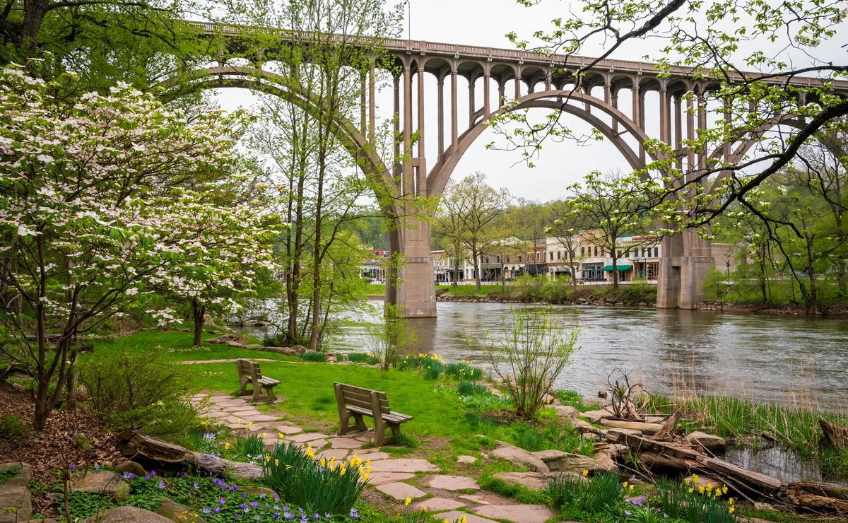 The Chagrin River flowing under a historic bridge in downtown Willoughby, Ohio, with a riverside park in spring